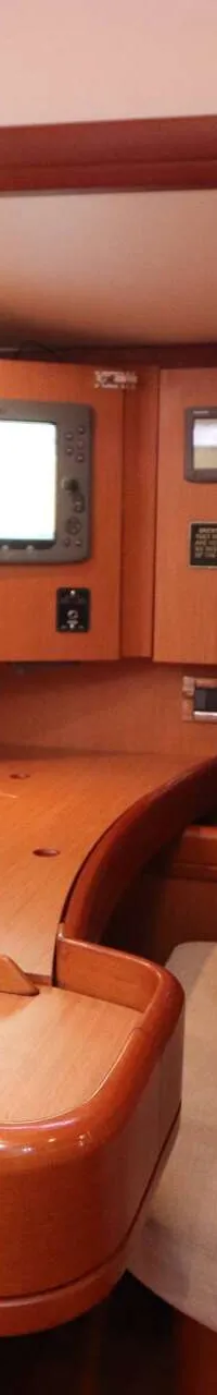 Een houten interieur van een boot met een navigatietafel, een bank met witte kussens en diverse elektronische apparatuur.