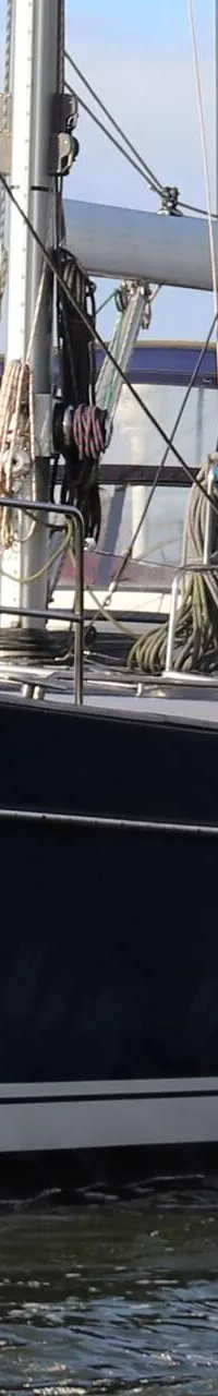 Een donkerblauwe zeilboot met witte strepen op de romp vaart op water, met een oranje vlag aan de achtersteven. — Beneteau 57