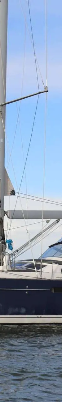 Een donkerblauwe zeilboot met witte strepen op de romp vaart op water onder een blauwe lucht. — Beneteau 57
