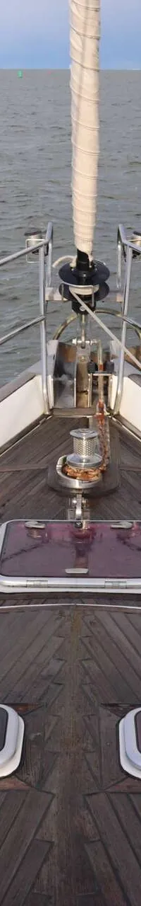 De foto toont het voordek van een zeilboot met een houten dek, reling en drie luiken, varend op water. — Beneteau 57