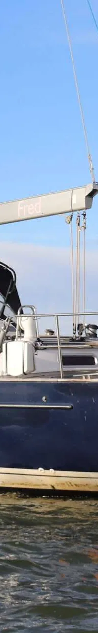 Een blauw-witte zeilboot met de naam "Fred" op de spiegel, ligt op het water onder een heldere hemel. — Beneteau 57