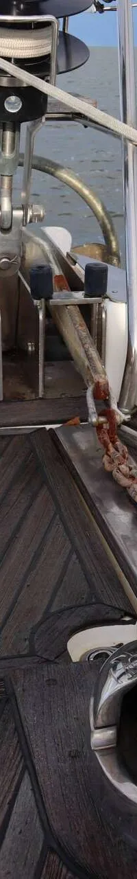 De boeg van een boot met een ankerlier, ankerketting, anker en een rolfokinstallatie, met water op de achtergrond.