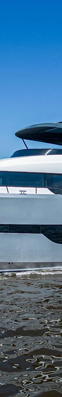 Een grote, grijze motorboot met een witte opbouw vaart op een waterweg onder een helderblauwe lucht.