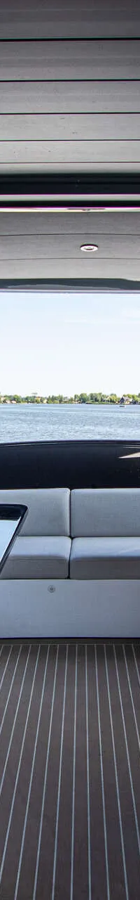 De foto toont het interieur van een boot met een stuurstand, zitplaatsen, een tafel en uitzicht op water en landschap.
