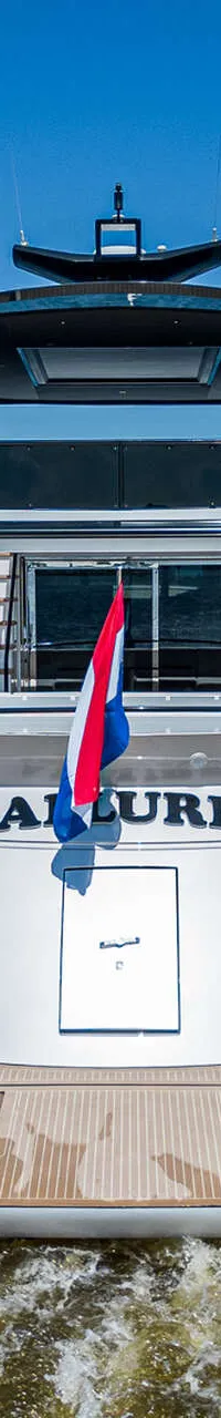 Een luxe motorjacht met de naam "ALLURE" vaart op een waterweg onder een helderblauwe lucht.