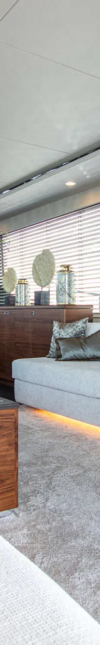 De foto toont een modern interieur met twee lichte banken, een houten salontafel met bloemen en ramen met jaloezieën.