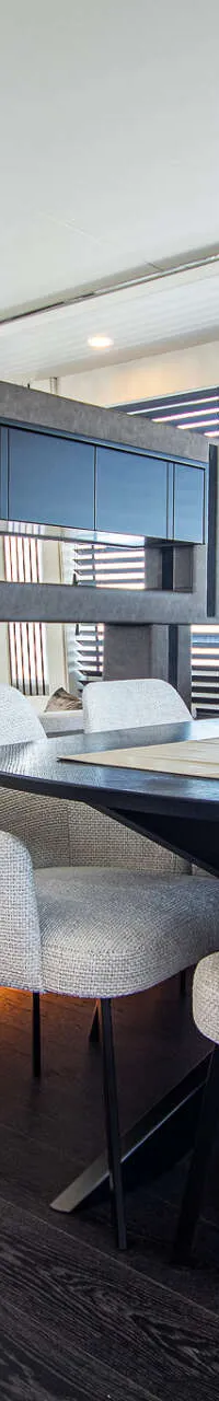 Een interieur van een boot met een eettafel met vier stoelen, een bank, een salontafel en een schuifdeur naar buiten.