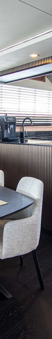 Een interieur van een boot met een eettafel, stoelen, een keukenblok en een trap naar beneden. — Van der Heijden Phantom 80
