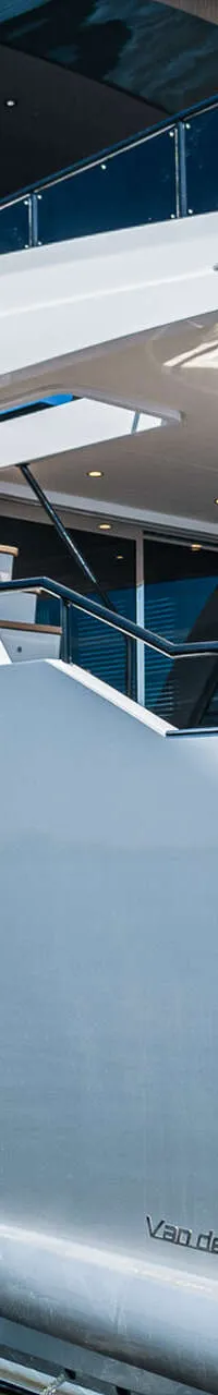 Een grote, zilverkleurige motorboot met donkere ramen en een flybridge ligt in het water onder een blauwe lucht.