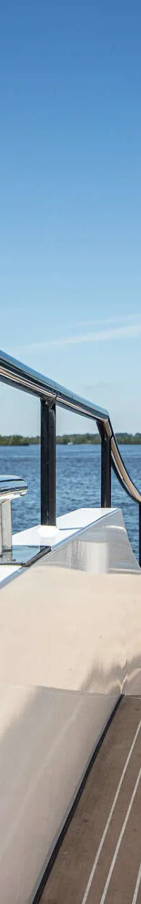 Een deel van het dek van een jacht met een reling, uitzicht op water en land, en het logo "DE VALK YACHT BROKERS".