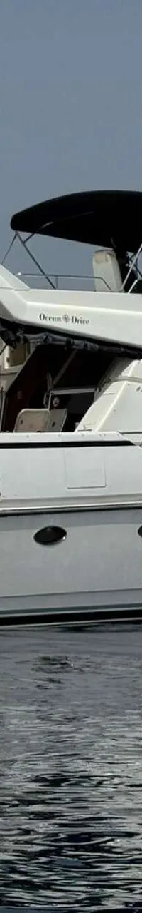 Een witte motorjacht met een zwarte bimini en een bijboot aan de achterzijde, drijvend op rustig water.