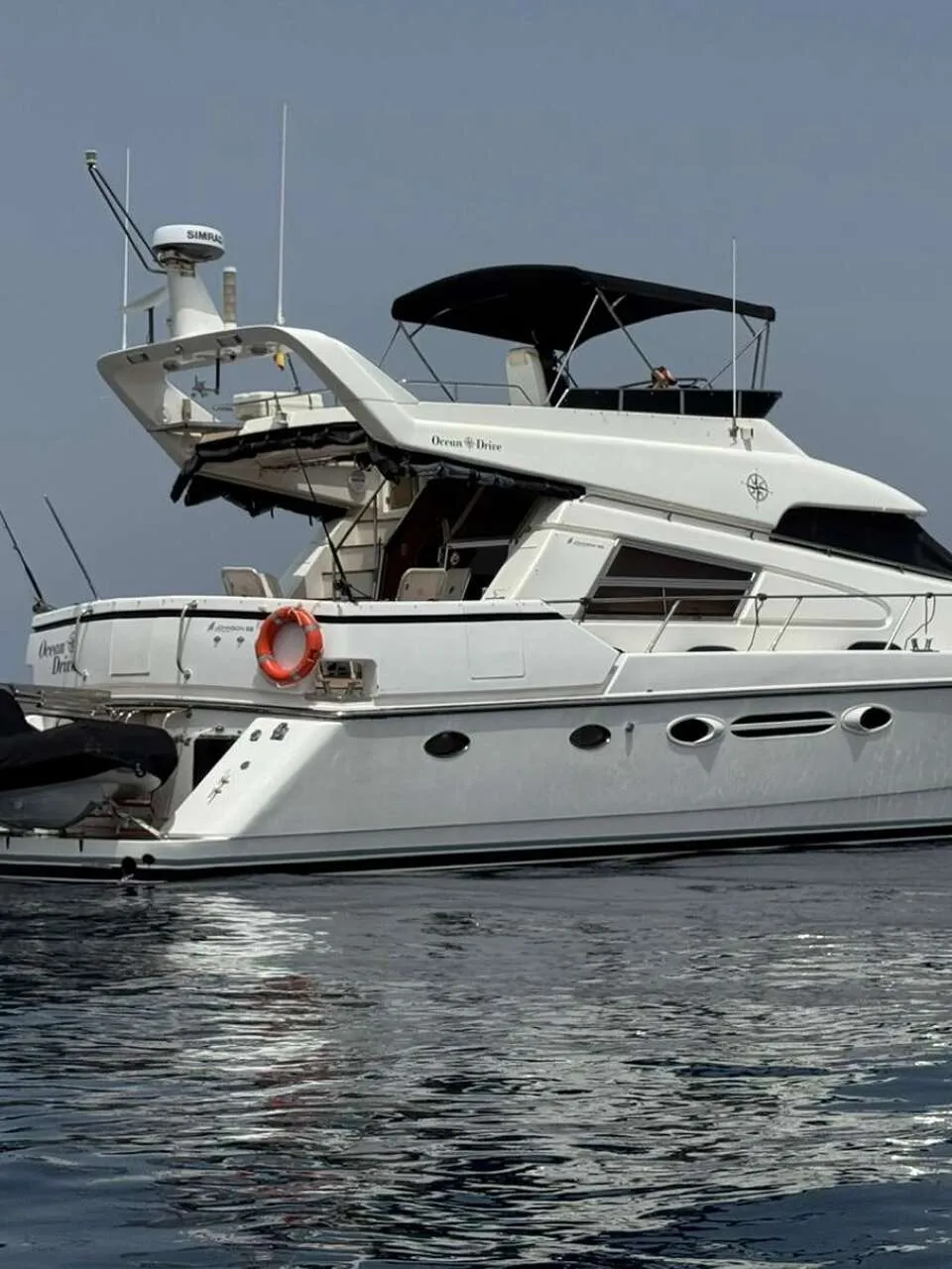 Een witte motorjacht met een zwarte bimini en een bijboot aan de achterzijde, drijvend op rustig water.