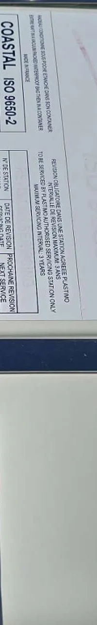Een witte reddingsvlotcontainer met een Plastimo Coastal ISO 9650-2 label en instructies.