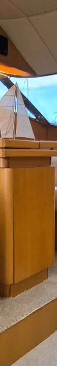 De foto toont het interieur van een boot met een zithoek, een tafel met een decoratief zeilbootje, en een keukenblok.