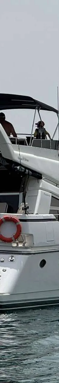 Een witte motorboot met de naam "Ocean Drive" op de spiegel, een bijboot en twee personen op het bovendek. — Johnson 56
