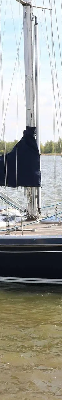 Een donkerblauwe zeilboot met een Nederlandse vlag vaart op een waterweg met een man aan het roer. — Victoire 1270