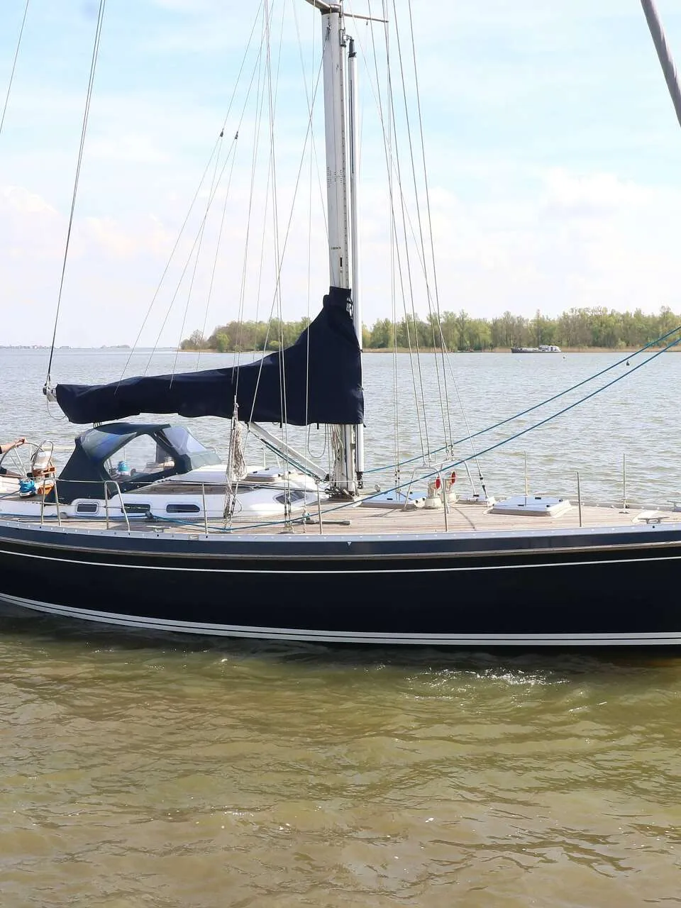 Een donkerblauwe zeilboot met een Nederlandse vlag vaart op een waterweg met een man aan het roer. — Victoire 1270