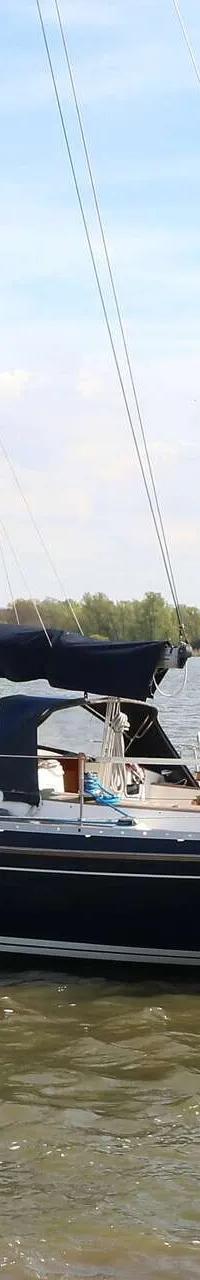 Een donkerblauwe zeilboot met een Nederlandse vlag en de naam "Indigo" op de spiegel, vaart op open water. — Victoire 1270