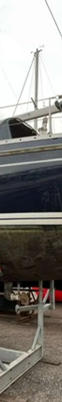 Een donkerblauwe zeilboot staat op een trailer op het droge, met een logo van "DE VALK YACHT BROKERS" rechtsboven.