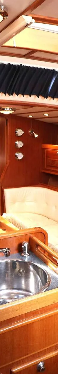 De foto toont het interieur van een boot met houten afwerking, zitbanken, een kombuis met twee spoelbakken en een…