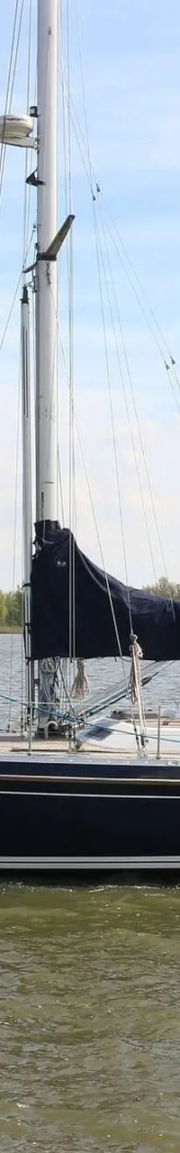 Een donkerblauwe zeilboot met een witte streep op de romp vaart op een waterweg met bomen op de achtergrond. — Victoire 1270