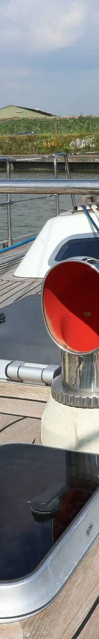 Een teakdek met twee rode ventilatiekappen, een luik en diverse lijnen en relingen.