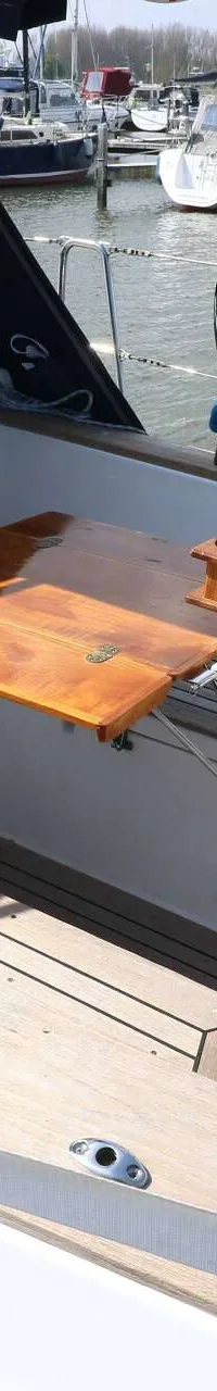 Een bovenaanzicht van de cockpit van een zeilboot met een stuurwiel, navigatie-instrumenten en een houten klaptafel.