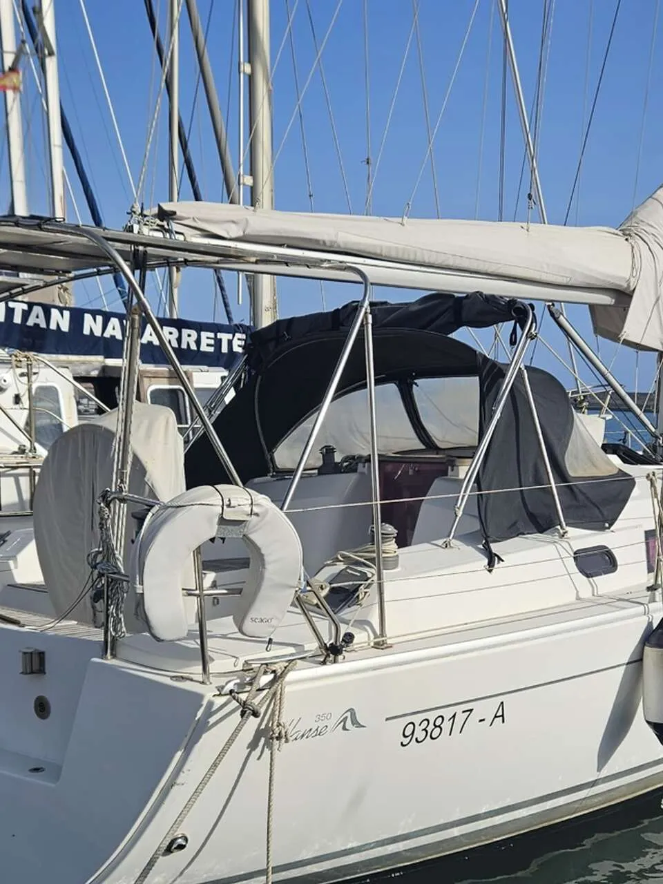 Een witte zeilboot met een zwarte buiskap en bimini ligt aangemeerd, met de registratie "93817-A" en "Hanse 350" op de romp.