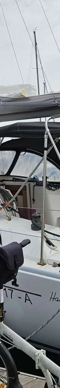 Een witte zeilboot met een zwarte buiskap en bimini ligt aangemeerd aan een houten steiger, met een vouwfiets op de…