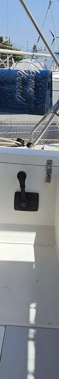 Een zwart stuurwiel en een houten dek zijn zichtbaar op een boot, met andere boten en een ladder op de achtergrond.