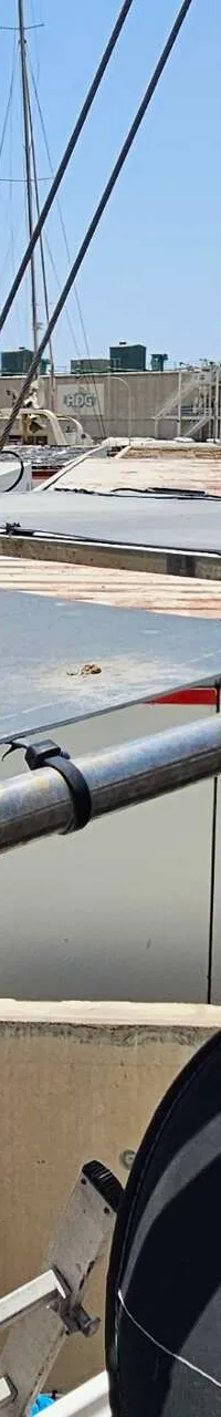Een bovenaanzicht van een bootdek met zonnepanelen, een brandblusser-pictogram en een cementfabriek op de achtergrond.