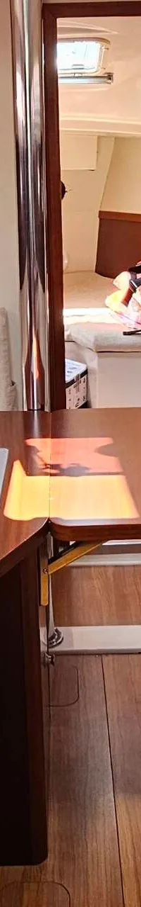 Een interieur van een boot met een houten tafel, banken met lichte kussens, een gootsteen en een doorgang naar een andere…
