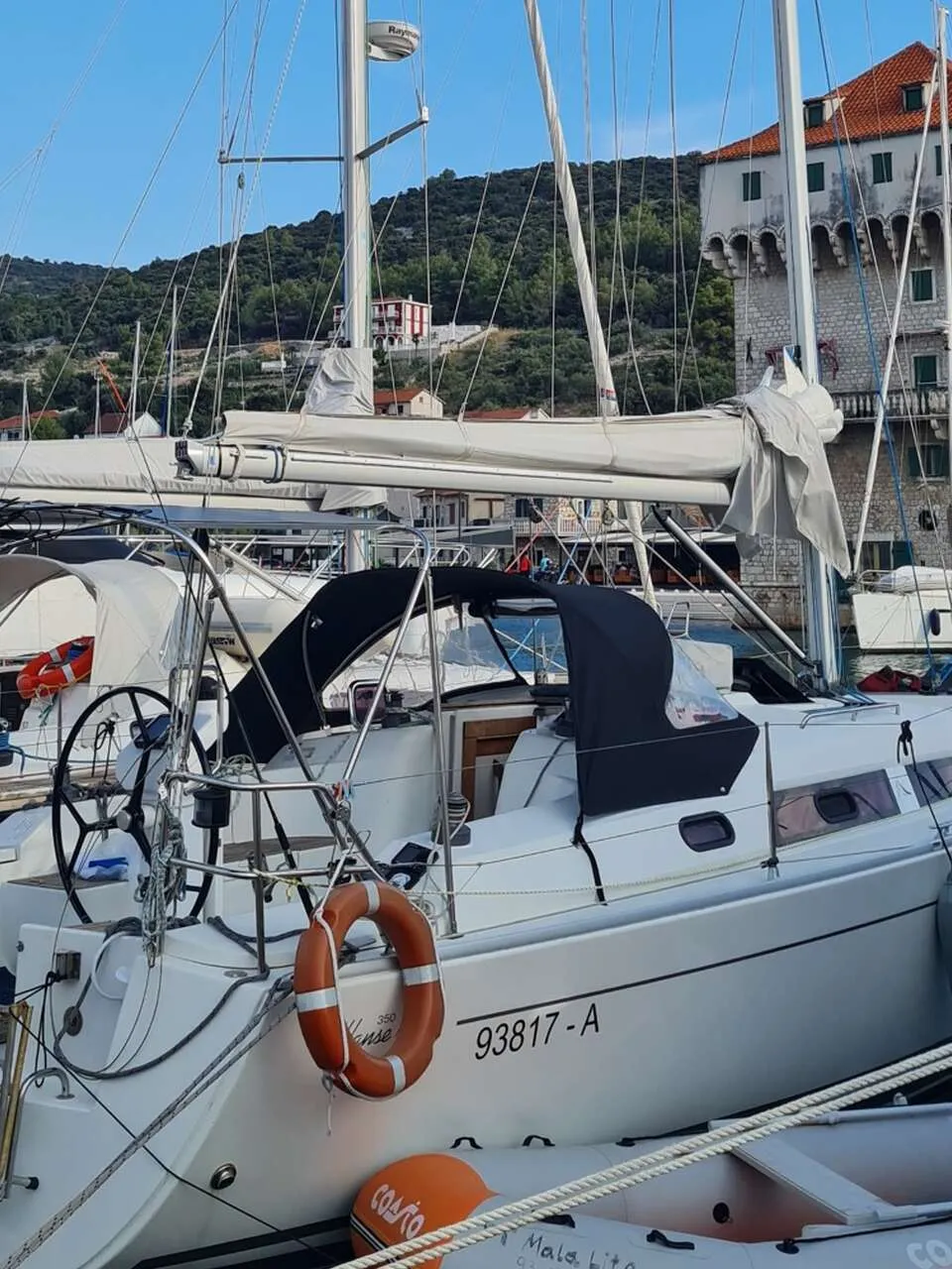 Een witte zeilboot met een zwarte buiskap en een reddingsboei ligt aangemeerd in een haven. — Hanse 350