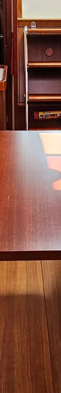 De foto toont een interieur van een boot met een houten tafel, banken met lichte bekleding, een kombuis en een trapje.