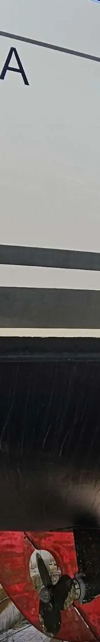 Een witte boot met zwarte strepen en een zwarte onderkant staat op de wal, met een rood roer en schroef. — Hanse 350