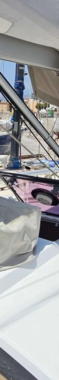 Een bovenaanzicht van het dek van een zeilboot met een open luik, touwen en een afdekzeil, omringd door andere boten.