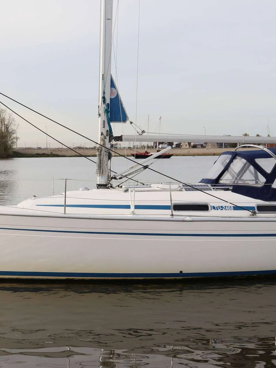 Een witte zeilboot met blauwe strepen en een blauwe buiskap ligt in het water. — Bavaria 31