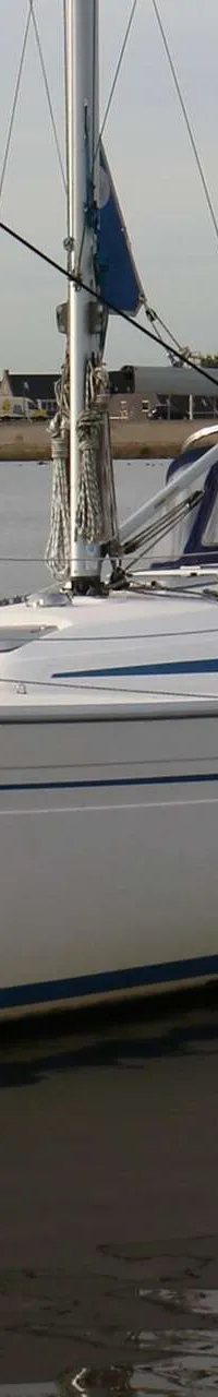 Een witte zeilboot met blauwe strepen ligt in het water, met een gele boei ernaast en land op de achtergrond. — Bavaria 31