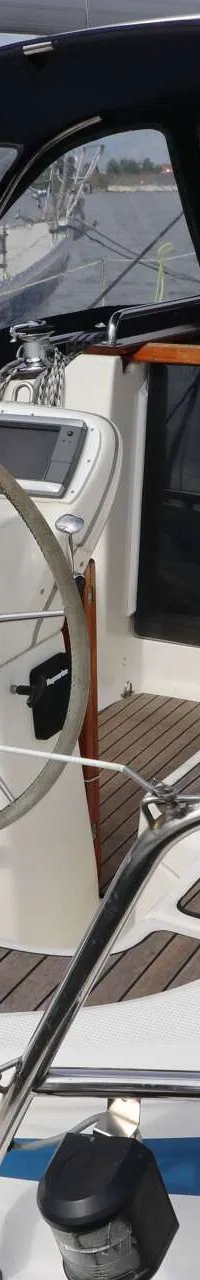 Een witte zeilboot met blauwe accenten en een donkerblauwe buiskap, met een stuurwiel en houten dekdelen. — Bavaria 31