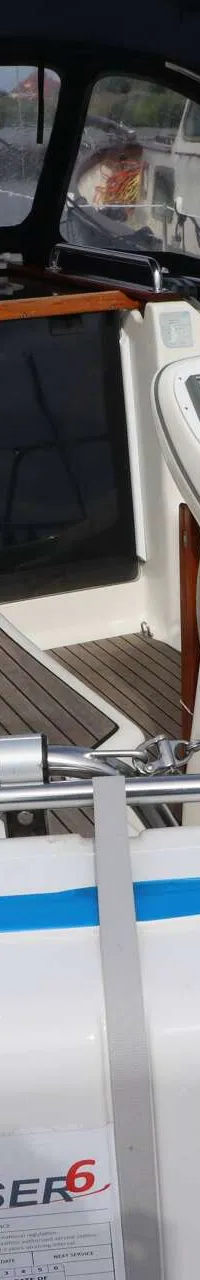 Een witte zeilboot met een blauwe buiskap, stuurwiel en een reddingsvlot aan de achterzijde. — Bavaria 31