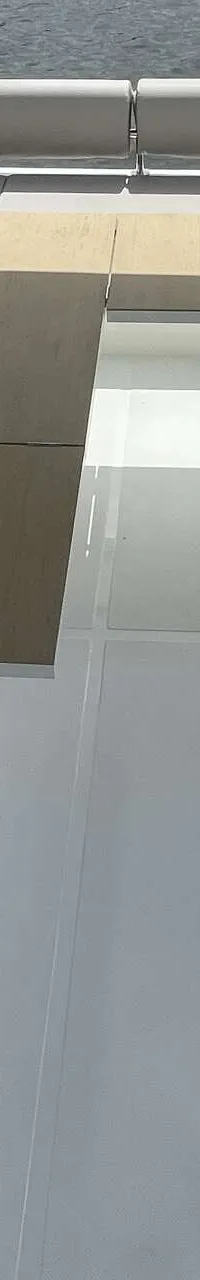 Een bovenaanzicht van een bootdek met grijze kussens, een houten tafel en een open luik met trap.