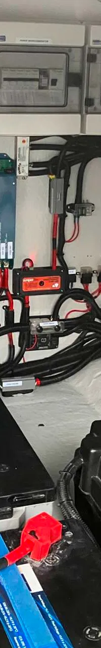 De foto toont een detail van de technische installatie van een boot, met accu's, omvormers, zekeringkasten en diverse…