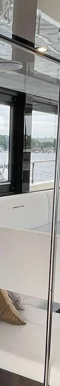 De foto toont het interieur van een boot met een keukenblok, een zithoek met tafel en uitzicht op water en een andere boot.