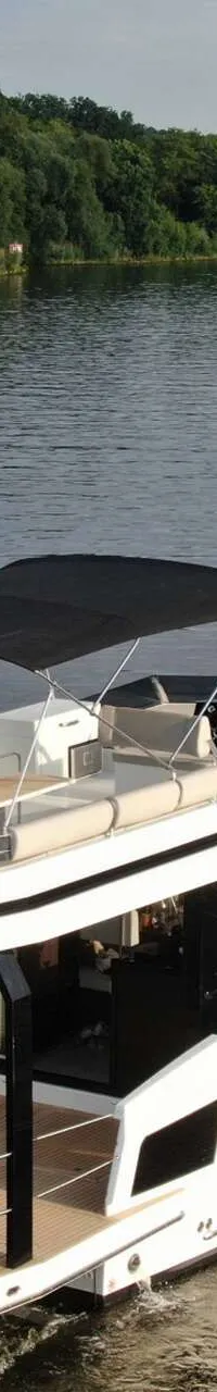 Een witte motorboot met een zwart zonnedek vaart op een waterweg met beboste oevers. — Cobra Yachts Maestro 42