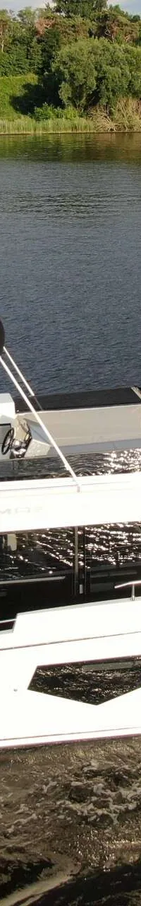 Een witte motorboot met een zwarte bimini en een persoon aan boord vaart op een waterweg met bomen op de achtergrond.