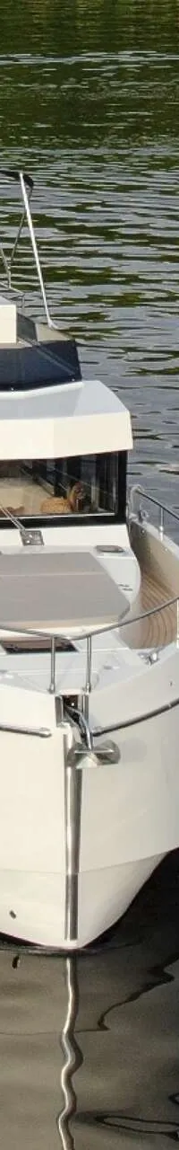 Een witte motorboot met een zwarte bimini vaart op rustig water, met een logo van "DE VALK YACHT BROKERS" rechtsboven.
