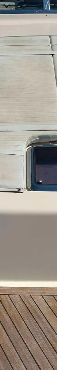 Een bovenaanzicht van het voordek van een boot met een teakhouten dek, een beige opbouw en een zonnedek met patrijspoort.