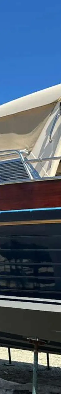 Een donkerblauwe boot met een houten bovenrand en een beige kap staat op bokken onder een helderblauwe lucht.