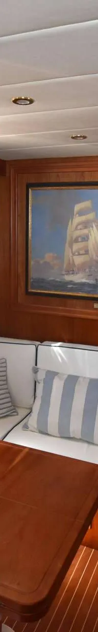 De foto toont een kajuit met een houten interieur, een zithoek met witte kussens en gestreepte kussens, een tafel, een…
