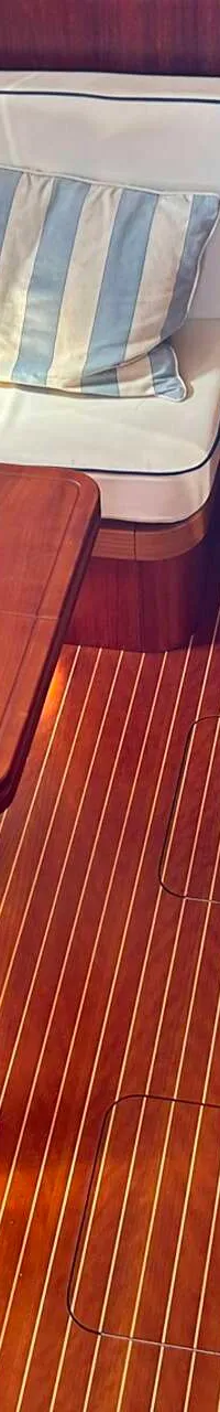 Een interieur van een boot met houten vloer en wanden, een bank met kussens en een tafel. — Apreamare 12 Cabinato